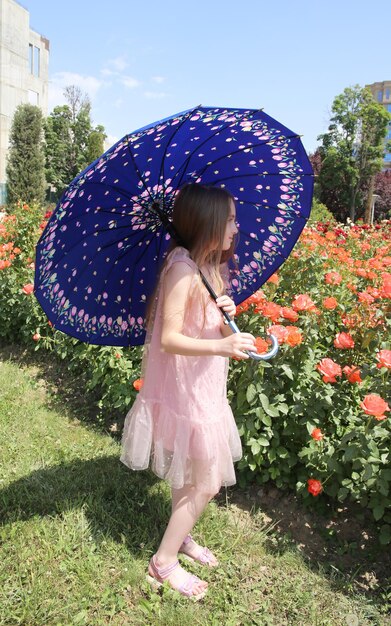 Kleines Mädchen mit blauem Regenschirm im Rosengarten