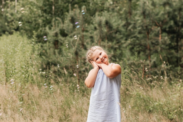 Kleines Mädchen mit blonden Haaren spielt im Sommer mit Seifenblasen in der Familienaktivität im Park Fühlen Sie sich fröhlich und fröhlich und genießen Sie es, während des Sonnenstrahls im Garten zu spielen
