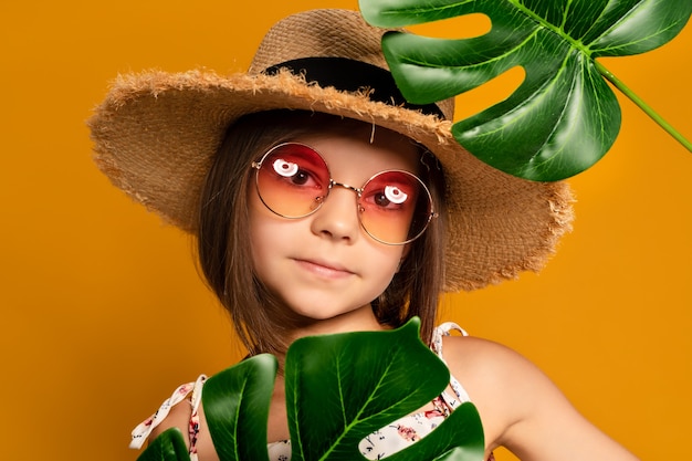 kleines Mädchen mit Brille und Strohhut auf gelbem Hintergrund im Studio