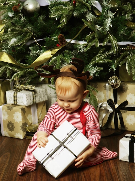 Kleines Mädchen mit der Geschenkbox in der Nähe Weihnachtsbaum schmücken Glückliche Zeit