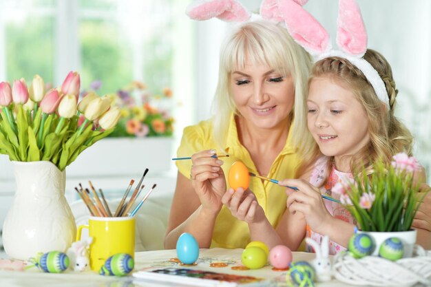 Kleines Mädchen mit der Mutter, die Eier für Osterferien malt