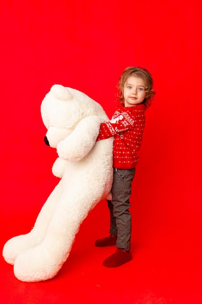 Kleines Mädchen mit einem großen Teddybär in Winterkleidung auf rotem Hintergrund Platz für Text