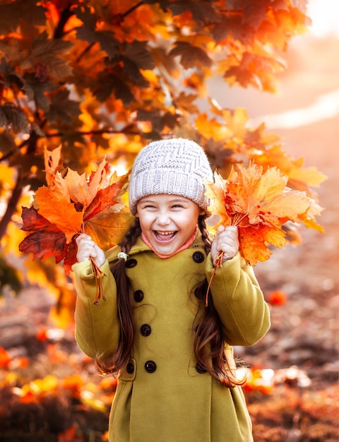 Kleines Mädchen mit einem Herbststrauß von Blättern in ihren Händen lacht