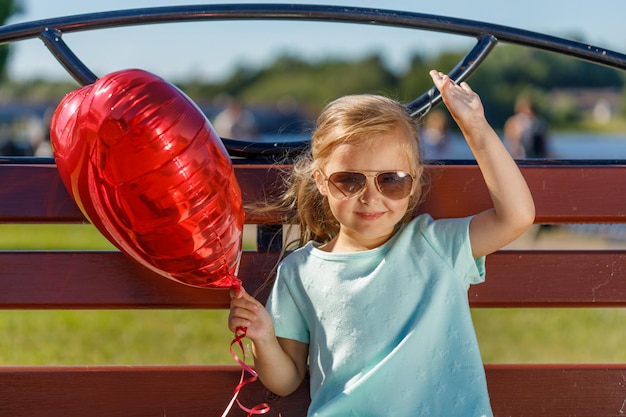 Kleines Mädchen mit einem herzförmigen Ballon in der Natur