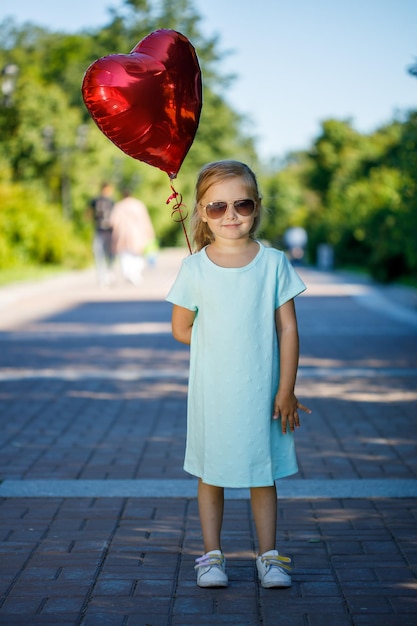 Kleines Mädchen mit einem herzförmigen Ballon in der Natur