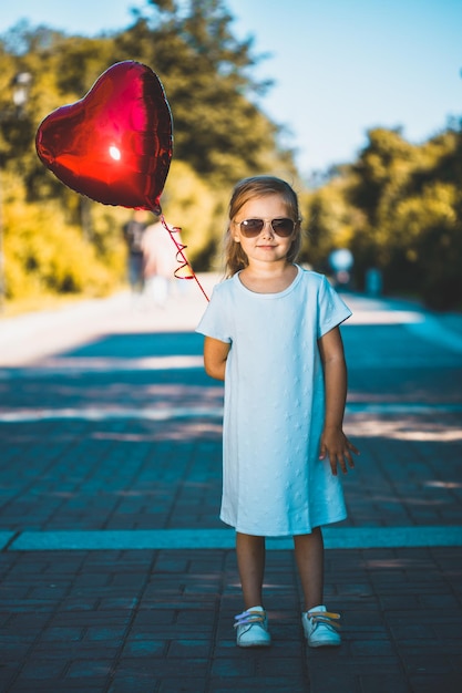 Kleines Mädchen mit einem herzförmigen Ballon in der Natur