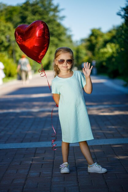 Kleines Mädchen mit einem herzförmigen Ballon in der Natur