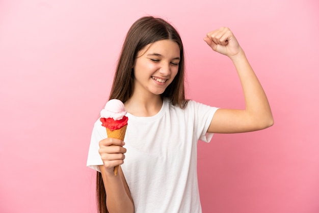 Kleines Mädchen mit einem Kornett-Eis über isoliertem rosa Hintergrund, das einen Sieg feiert