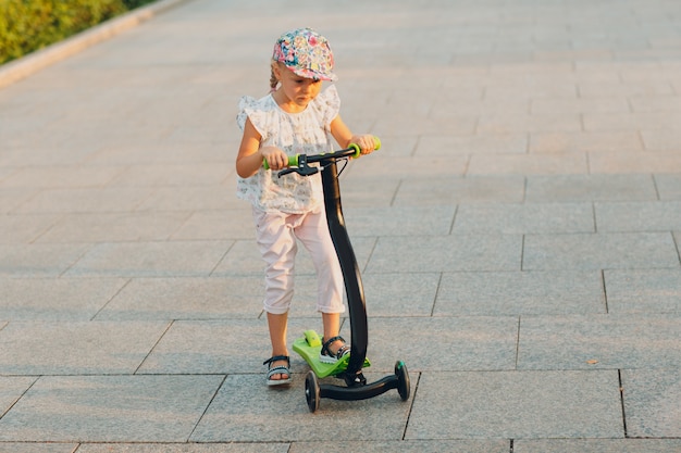 Kleines Mädchen mit einem Roller auf der Stadtstraße.