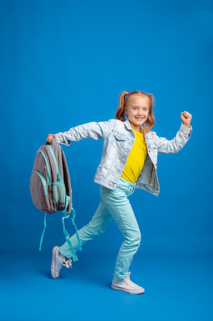 Kleines Mädchen mit einem Rucksack in voller Länge auf blauem Hintergrund