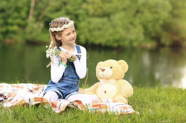 Kleines Mädchen mit einem Stofftier auf einem Picknick nahe dem Fluss an einem sonnigen Tag