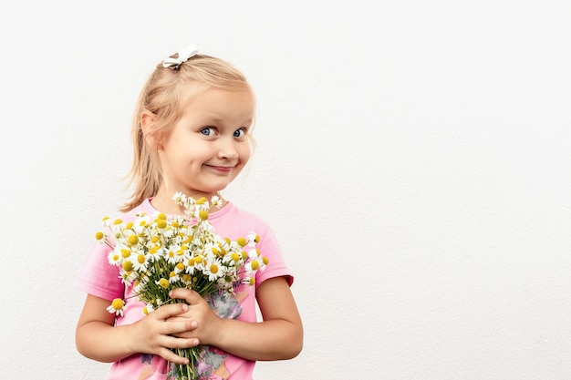 Kleines Mädchen mit einem Strauß Gänseblümchen in den Händen auf weißem Hintergrund