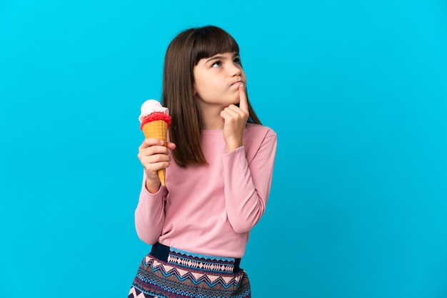 Kleines Mädchen mit einer Kornett-Eiscreme isoliert, die Zweifel beim Aufblicken hat