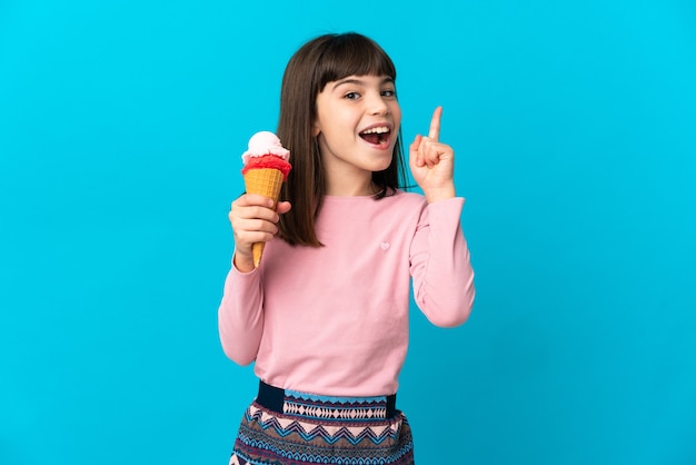 Kleines Mädchen mit einer Kornett-Eiscreme lokalisiert auf blauer Wand, die eine Idee denkt, die den Finger nach oben zeigt