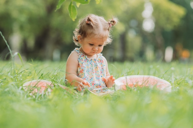 Kleines Mädchen mit einer lustigen Frisur isst eine Wassermelone auf dem Rasen im Park gesunder Snack für Kinder