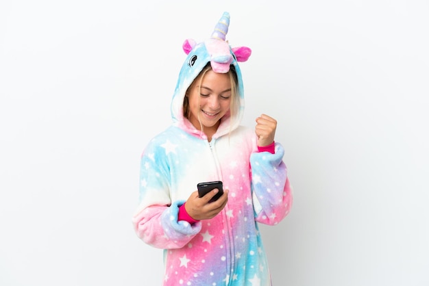 Kleines Mädchen mit Einhorn-Pyjama isoliert auf weißem Hintergrund mit Telefon in Siegesposition