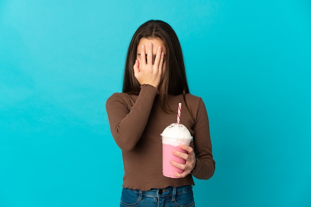 Kleines Mädchen mit Erdbeermilchshake lokalisiert auf blauem Hintergrund mit müde und krankem Ausdruck