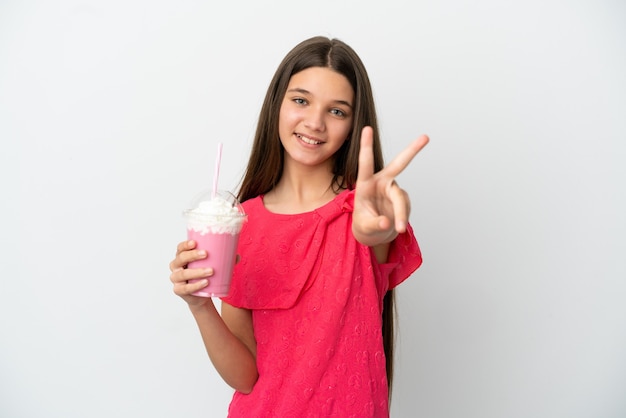 Kleines Mädchen mit Erdbeermilchshake über isoliertem weißem Hintergrund lächelt und zeigt Victory-Zeichen
