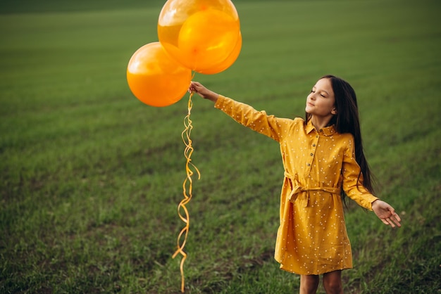 Kleines Mädchen mit gelben Luftballons auf dem Gebiet