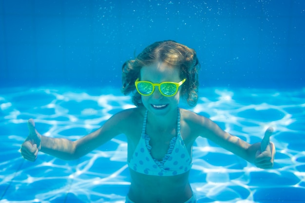 Kleines Mädchen mit gelber Sonnenbrille unter Wasser im Schwimmbad