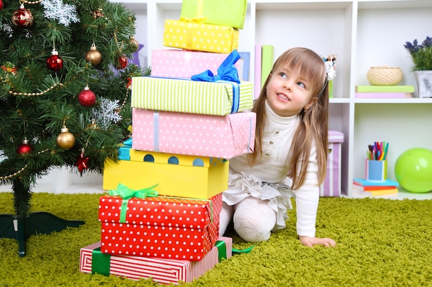 Kleines Mädchen mit Geschenken nahe Weihnachtsbaum im Zimmer Christmas