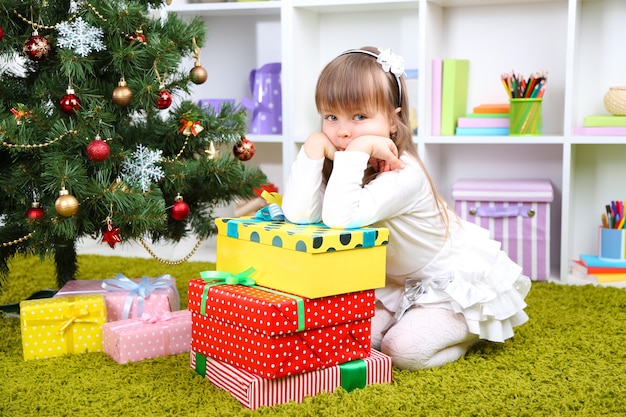 Kleines Mädchen mit Geschenken nahe Weihnachtsbaum im Zimmer Christmas