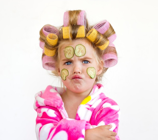 Kleines Mädchen mit Gurken im Gesicht. Mädchen in Lockenwicklern, Robe Kleine Kokette.