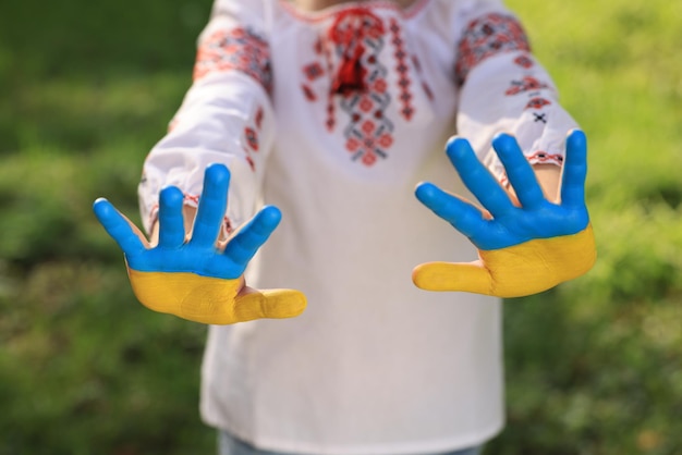 Kleines Mädchen mit Händen, die in der Farbe der ukrainischen Flagge bemalt sind, konzentriert sich im Freien auf Palmen Liebes-Ukraine-Konzept