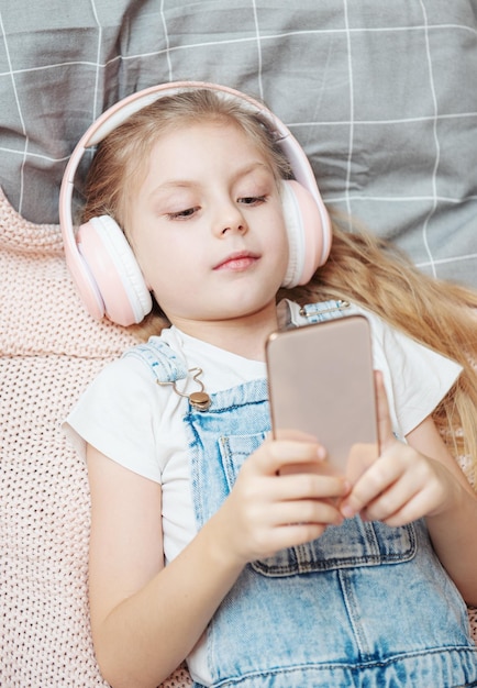 Kleines Mädchen mit Handy, das Musik hört, während es im Bett liegt