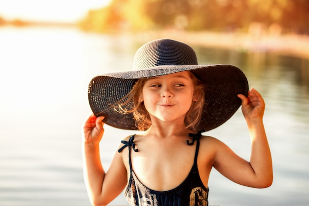 kleines Mädchen mit Hut am Fluss im Sommer