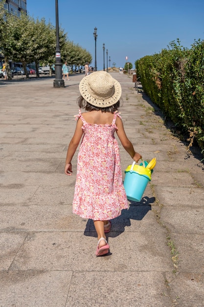 Kleines Mädchen mit Hut und Kleid und ihren Strandspielzeugen