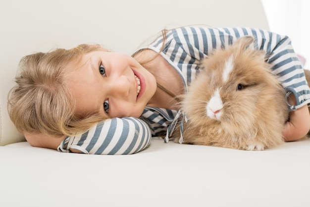 Kleines Mädchen mit ihrem Häschen, das auf dem Sofa liegt und sich umarmt