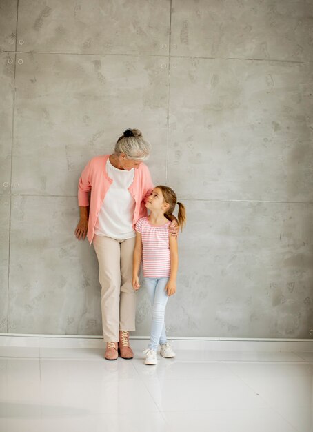 Kleines Mädchen mit ihrer Großmutter, die an der grauen Wand steht