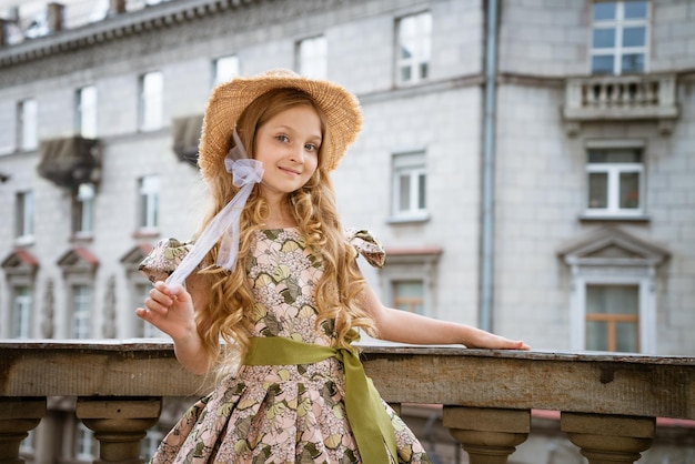 Kleines Mädchen mit Kleid und Hut posiert auf dem Balkon