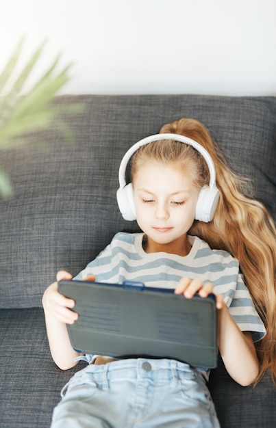 Kleines Mädchen mit Kopfhörern und Tablet zu Hause