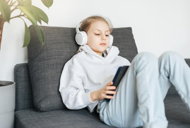 Kleines Mädchen mit Kopfhörern und Tablet zu Hause