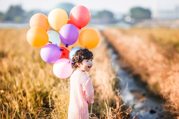 Kleines Mädchen mit Luftballons auf Weizenfeld spielen