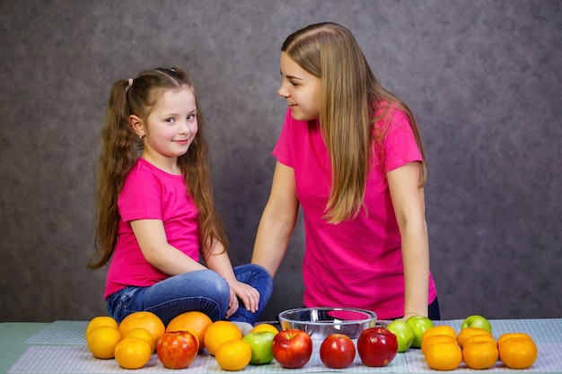 Kleines Mädchen mit Mama spielt mit Früchten und lächelt. Vitamine und gesunde Ernährung für Kinder.