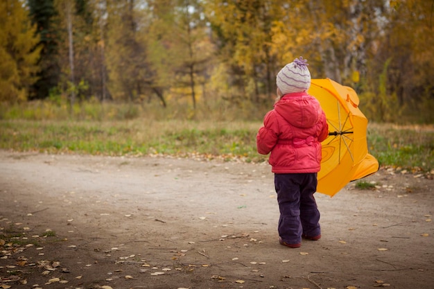 Kleines Mädchen mit Regenschirm im Herbst Park zurück