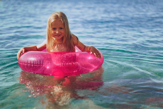 Kleines Mädchen mit rosa aufblasbarem Kreis, der im Meer badet