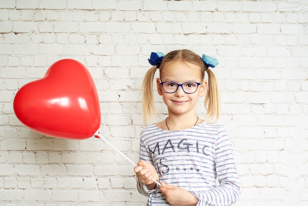 Kleines Mädchen mit rotem herzförmigem Ballon, Valentinstag