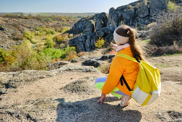 Kleines Mädchen mit Rucksack, das tagsüber auf einem Berggipfel steht