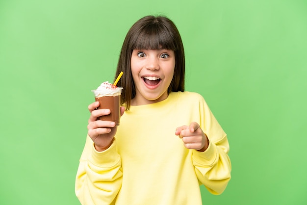 Kleines Mädchen mit Schokoladencreme über isoliertem Chroma-Key-Hintergrund überrascht und zeigt nach vorne