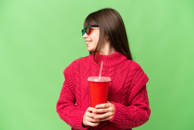 Kleines Mädchen mit Soda über isoliertem Chroma-Key-Hintergrund mit Blick auf die Seite