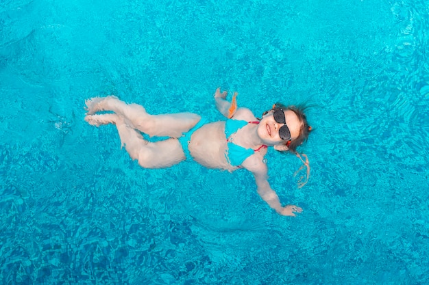 Kleines Mädchen mit Sonnenbrille schwimmt an einem Sommertag in einem Schwimmbad mit blauem Wasser