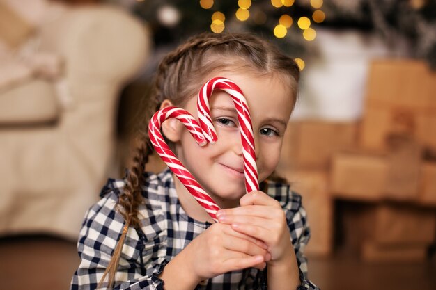 Kleines Mädchen mit süßen Weihnachtssüßigkeiten an Heiligabend im Wohnzimmer