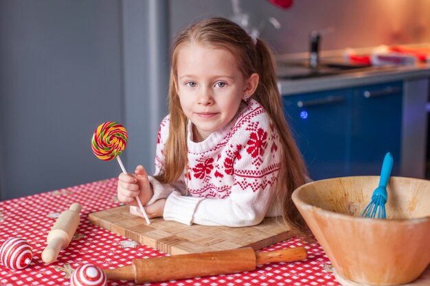 Kleines Mädchen mit Süßigkeit in der Hand bereitet Weihnachtskuchen zu