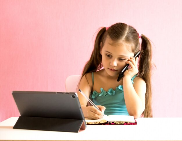 Kleines Mädchen mit Telefon und Tablette am Tisch