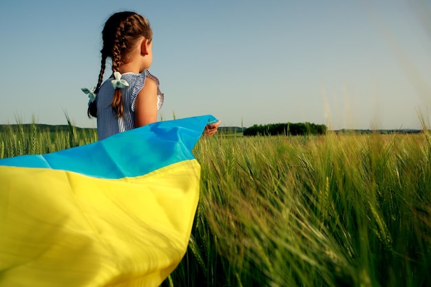 Kleines Mädchen mit ukrainischer Flagge im Weizenfeld Glücklicher Junge, der den Unabhängigkeitstag feiert