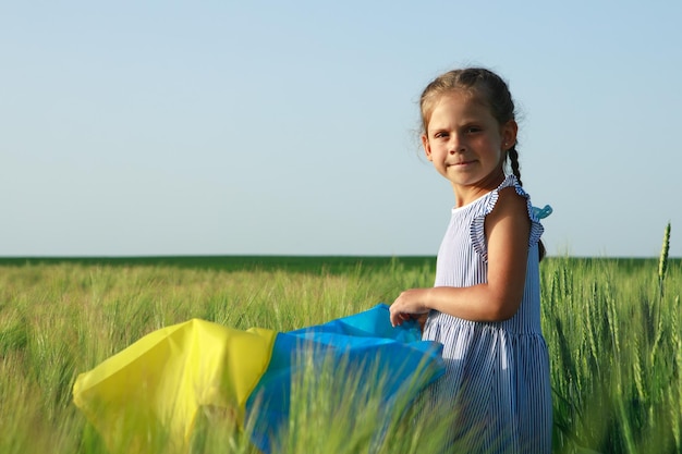 Kleines Mädchen mit ukrainischer Flagge im Weizenfeld Glücklicher Junge, der den Unabhängigkeitstag feiert